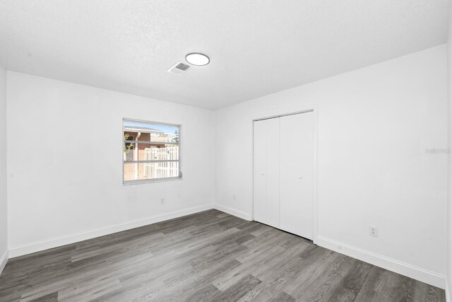 unfurnished bedroom featuring wood finished floors, visible vents, a closet, and baseboards