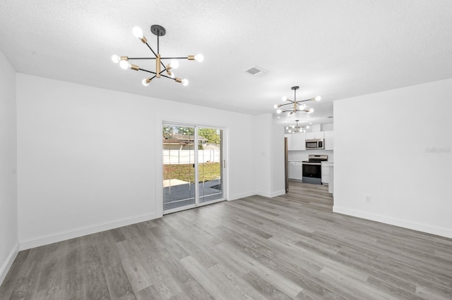 unfurnished living room with a textured ceiling, visible vents, a notable chandelier, and light wood finished floors