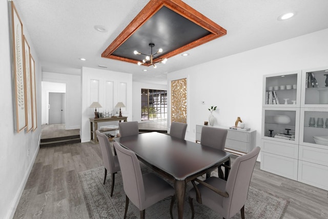 dining area featuring recessed lighting, light wood-type flooring, a raised ceiling, and baseboards