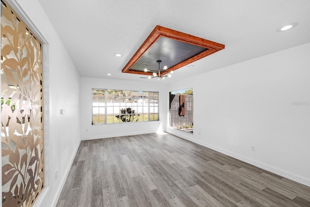 interior space with wood finished floors, baseboards, recessed lighting, a raised ceiling, and a notable chandelier