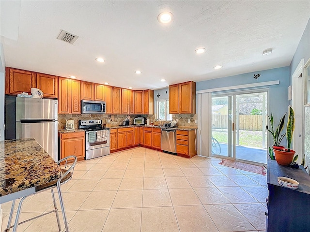 kitchen with visible vents, appliances with stainless steel finishes, brown cabinetry, light tile patterned floors, and decorative backsplash