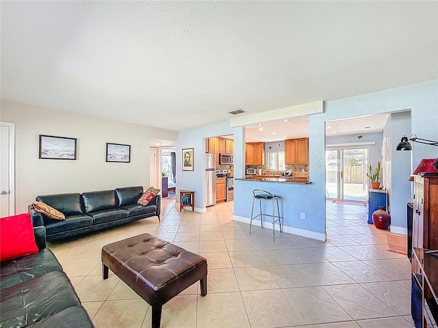 living area featuring light tile patterned floors, visible vents, baseboards, and a textured ceiling