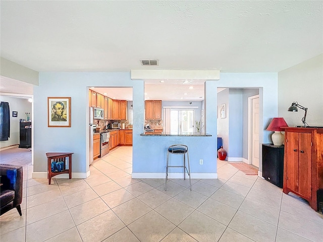 kitchen with dark countertops, visible vents, light tile patterned floors, brown cabinets, and appliances with stainless steel finishes