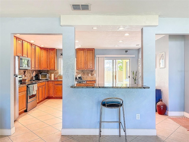 kitchen featuring visible vents, tasteful backsplash, stainless steel appliances, brown cabinetry, and light tile patterned floors