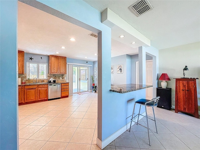 kitchen with visible vents, dishwasher, dark stone counters, brown cabinetry, and a sink