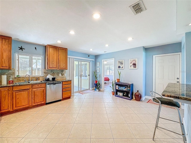 kitchen with visible vents, a sink, stainless steel dishwasher, brown cabinets, and backsplash