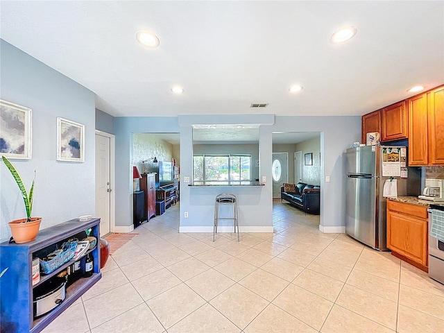 kitchen featuring baseboards, light tile patterned floors, recessed lighting, brown cabinets, and freestanding refrigerator