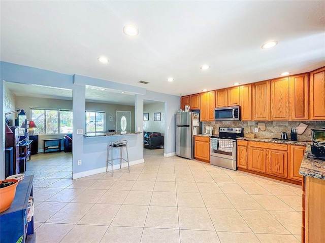 kitchen featuring light tile patterned floors, stainless steel appliances, brown cabinets, and tasteful backsplash