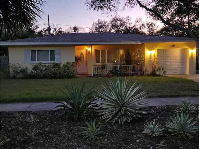 ranch-style house featuring a shingled roof, a porch, a front yard, stucco siding, and an attached garage