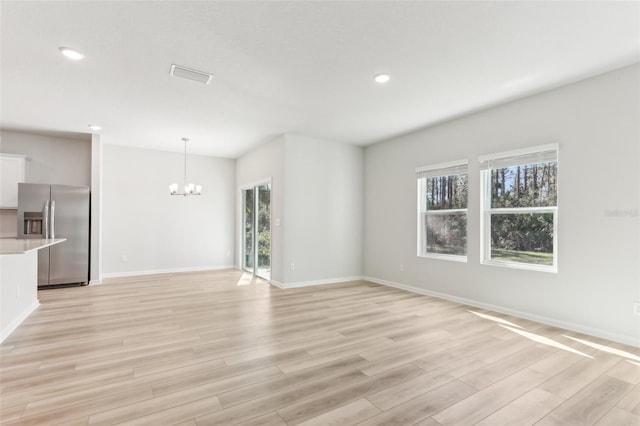 unfurnished living room featuring recessed lighting, baseboards, light wood finished floors, and a chandelier