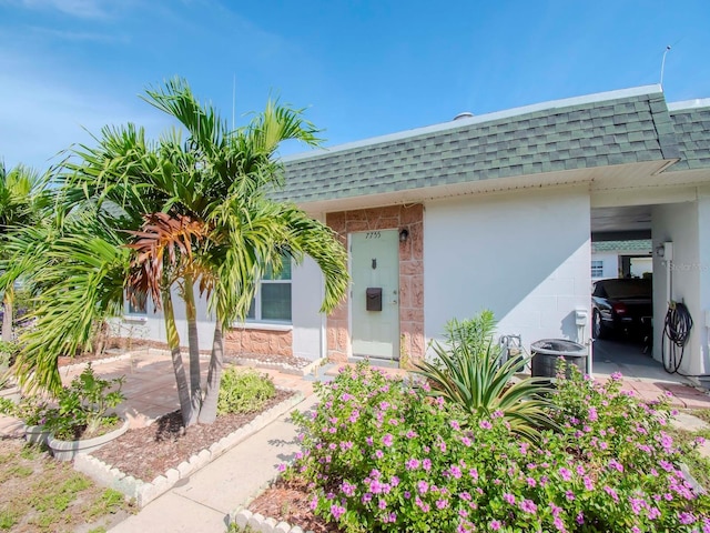 doorway to property with an attached carport, mansard roof, central AC, and roof with shingles