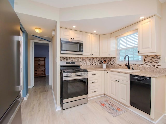 kitchen featuring a sink, stainless steel appliances, light wood-style floors, white cabinets, and decorative backsplash