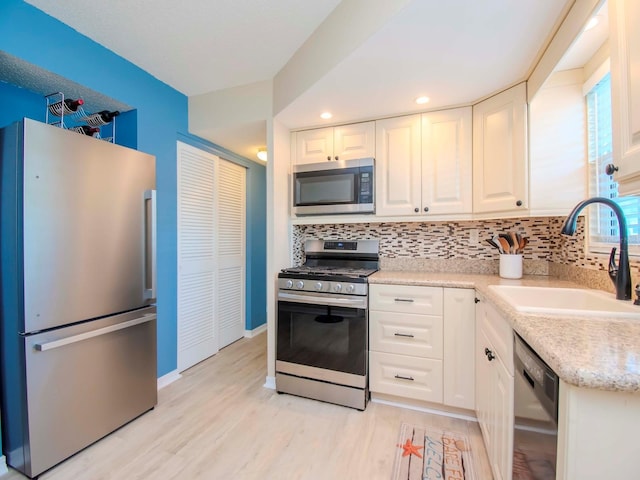 kitchen with light wood-type flooring, a sink, tasteful backsplash, stainless steel appliances, and white cabinets