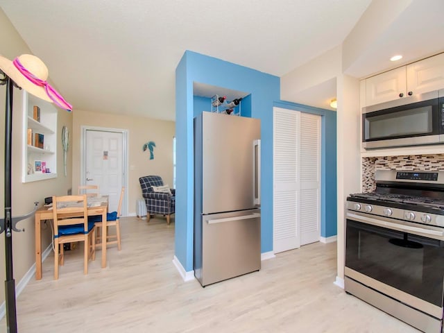 kitchen featuring decorative backsplash, white cabinetry, appliances with stainless steel finishes, and light wood-type flooring