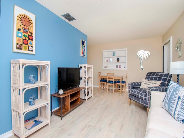 living area with visible vents, built in shelves, baseboards, and wood finished floors