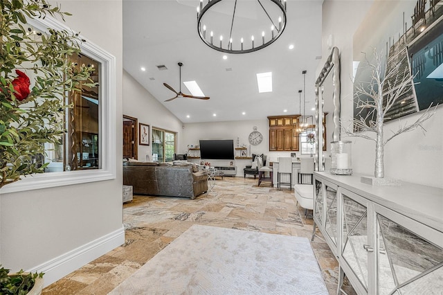 living area with stone tile floors, ceiling fan with notable chandelier, baseboards, and high vaulted ceiling