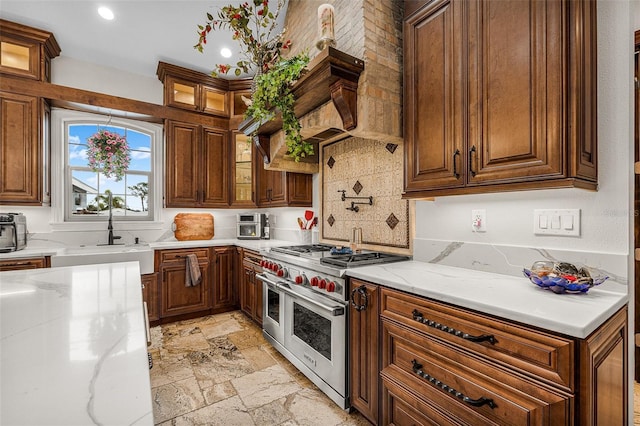 kitchen featuring stone tile flooring, double oven range, glass insert cabinets, and a sink