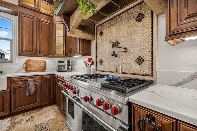 kitchen with light countertops, glass insert cabinets, double oven range, and stone tile flooring