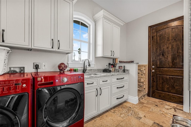 clothes washing area with washing machine and clothes dryer, cabinet space, stone finish flooring, and a sink