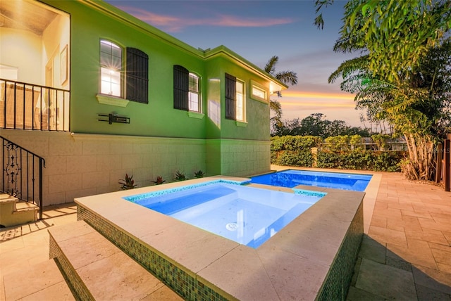 pool at dusk with an in ground hot tub, a fenced in pool, and a patio