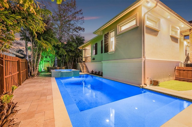 pool at dusk with stairs, a patio, a fenced backyard, and a pool with connected hot tub