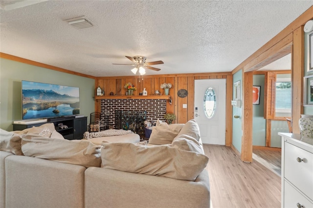 living area with visible vents, a ceiling fan, a textured ceiling, light wood-style floors, and a brick fireplace