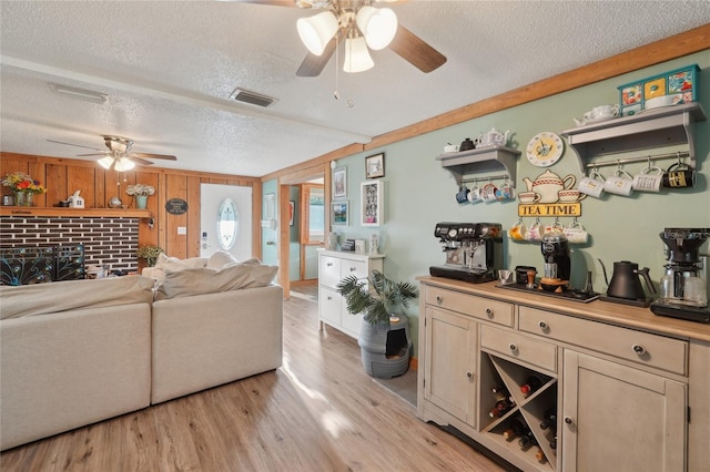 living area with visible vents, a brick fireplace, ceiling fan, light wood-type flooring, and a textured ceiling