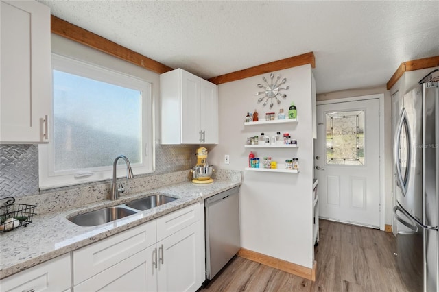 kitchen featuring light wood-style flooring, a sink, stainless steel appliances, white cabinets, and backsplash