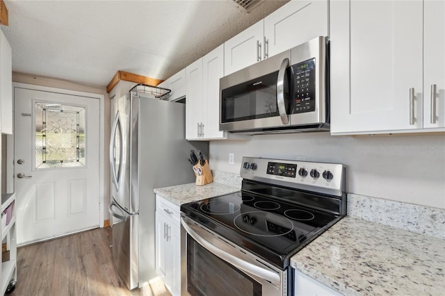 kitchen with white cabinets, light stone counters, light wood-type flooring, and appliances with stainless steel finishes