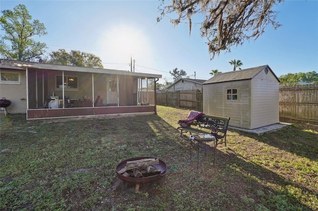 view of yard featuring a fire pit, a shed, a sunroom, an outdoor structure, and a fenced backyard