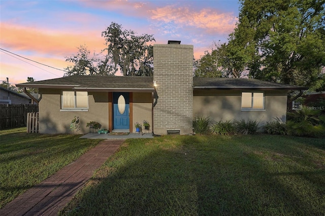 view of front facade featuring stucco siding, a chimney, a front yard, and fence