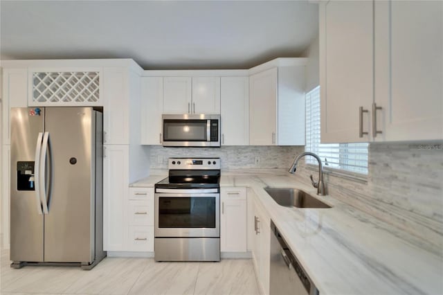 kitchen with a sink, light stone counters, appliances with stainless steel finishes, white cabinets, and decorative backsplash