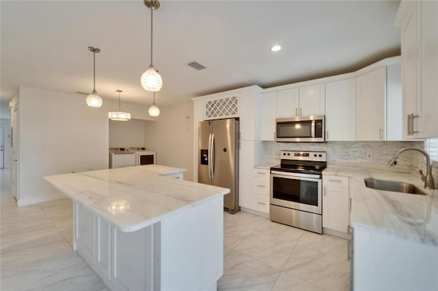 kitchen featuring independent washer and dryer, a sink, a center island, appliances with stainless steel finishes, and decorative backsplash