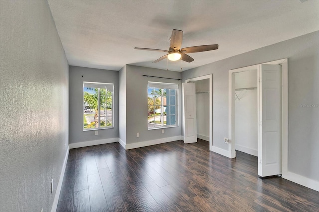 unfurnished bedroom with baseboards, two closets, dark wood-style floors, and a textured wall