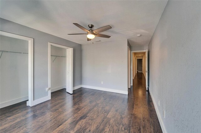 unfurnished bedroom featuring visible vents, multiple closets, a ceiling fan, baseboards, and dark wood-style flooring