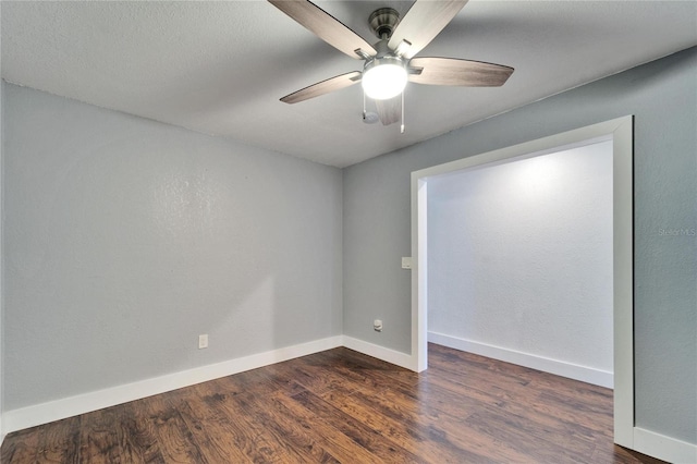 spare room featuring dark wood-style floors, a ceiling fan, and baseboards