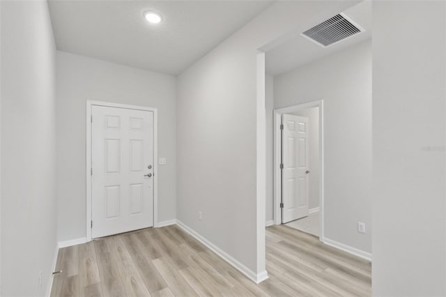 hall with light wood finished floors, visible vents, and baseboards