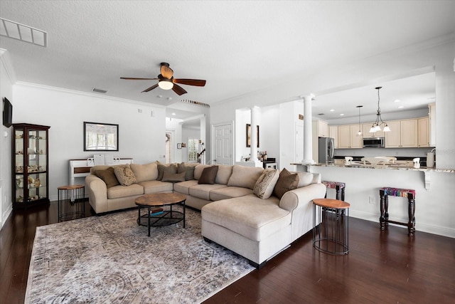 living room with visible vents, ornamental molding, ceiling fan with notable chandelier, dark wood finished floors, and ornate columns