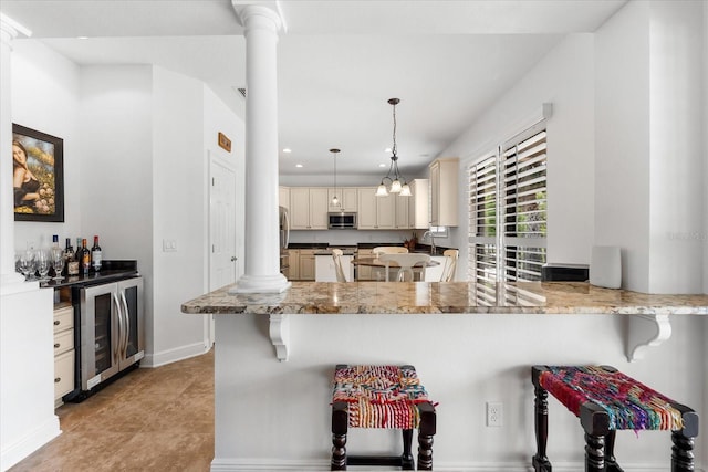 kitchen featuring cream cabinets, wine cooler, appliances with stainless steel finishes, a peninsula, and ornate columns