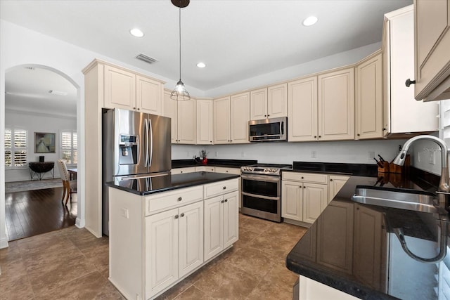 kitchen with dark countertops, stainless steel appliances, cream cabinets, and visible vents