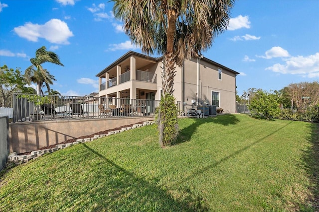 back of house featuring a yard, a balcony, stucco siding, and fence