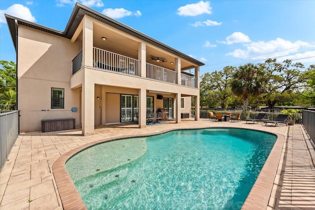 rear view of house with a balcony, a ceiling fan, fence, stucco siding, and a patio area