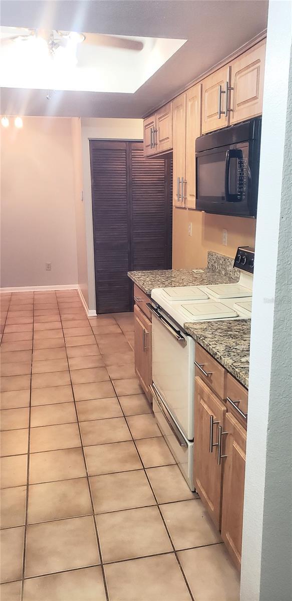 kitchen with white range with electric stovetop, light tile patterned floors, light brown cabinets, and black microwave