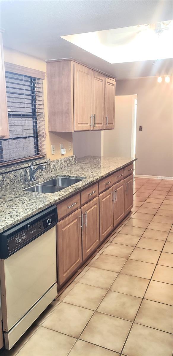 kitchen with baseboards, dishwasher, light stone counters, light tile patterned flooring, and a sink