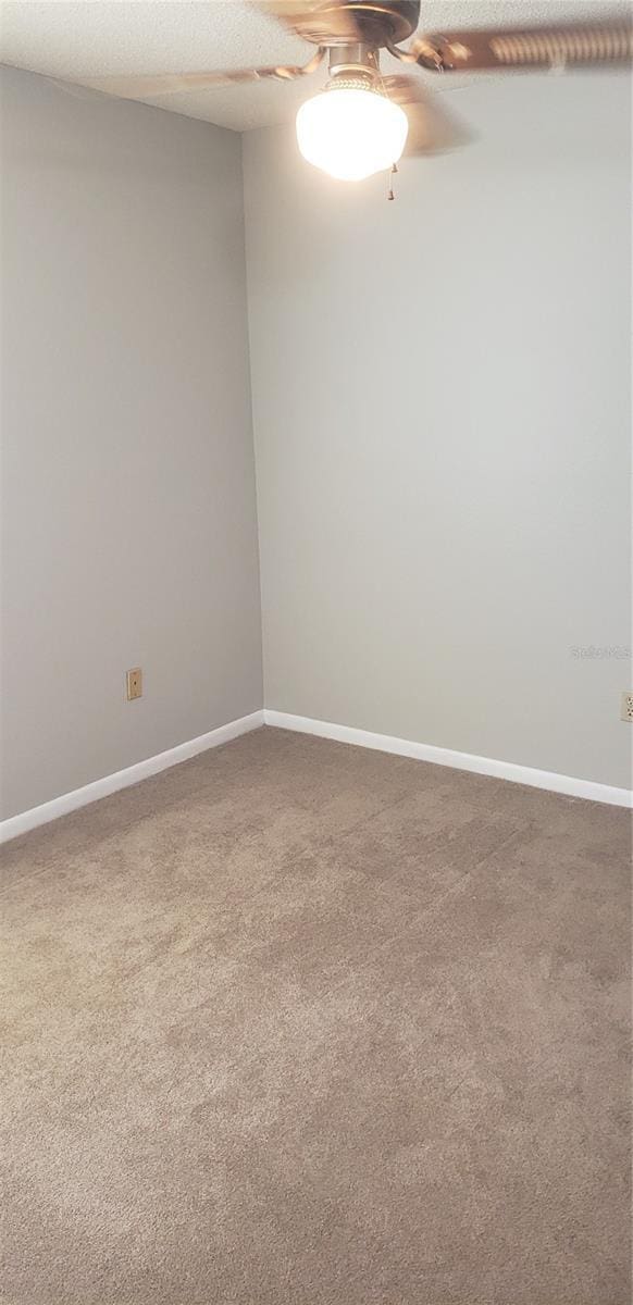 carpeted empty room with a ceiling fan and baseboards