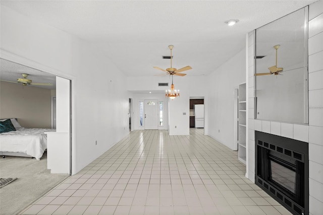 unfurnished living room with visible vents, light carpet, ceiling fan with notable chandelier, light tile patterned floors, and a tile fireplace