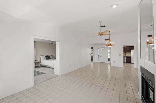 unfurnished living room with visible vents, light tile patterned flooring, a fireplace, vaulted ceiling, and ceiling fan with notable chandelier