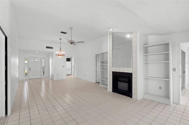 unfurnished living room with built in shelves, visible vents, a tile fireplace, a textured ceiling, and ceiling fan with notable chandelier