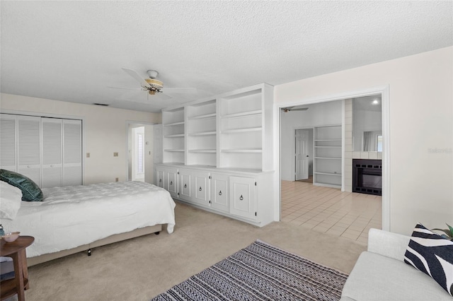 bedroom with visible vents, light colored carpet, a glass covered fireplace, a textured ceiling, and a ceiling fan