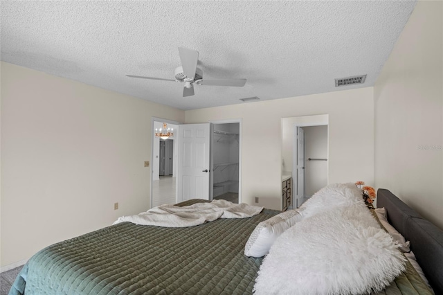 bedroom with visible vents, a closet, a textured ceiling, a walk in closet, and ceiling fan with notable chandelier